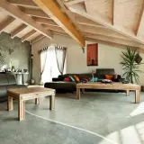 Nowoczesny salon z drewnianym sufitem i podłogą żywiczną. Skórzana kanapa, drewniane stoliki i rośliny tworzą przytulną atmosferę.