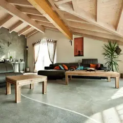 Nowoczesny salon z drewnianym sufitem i podłogą żywiczną. Skórzana kanapa, drewniane stoliki i rośliny tworzą przytulną atmosferę.