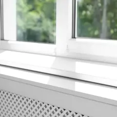Biały parapet pod okno, z widocznym fragmentem grzejnika, odbija światło słoneczne.