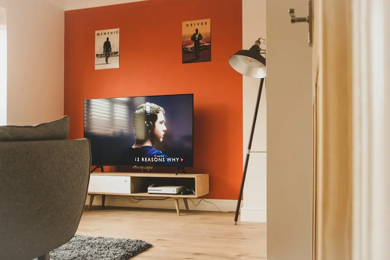 Pomarańczowe ściany świetnie komponują się z szarością kanapy i dywanu. W salonie wisi plakat z filmu "Driver".