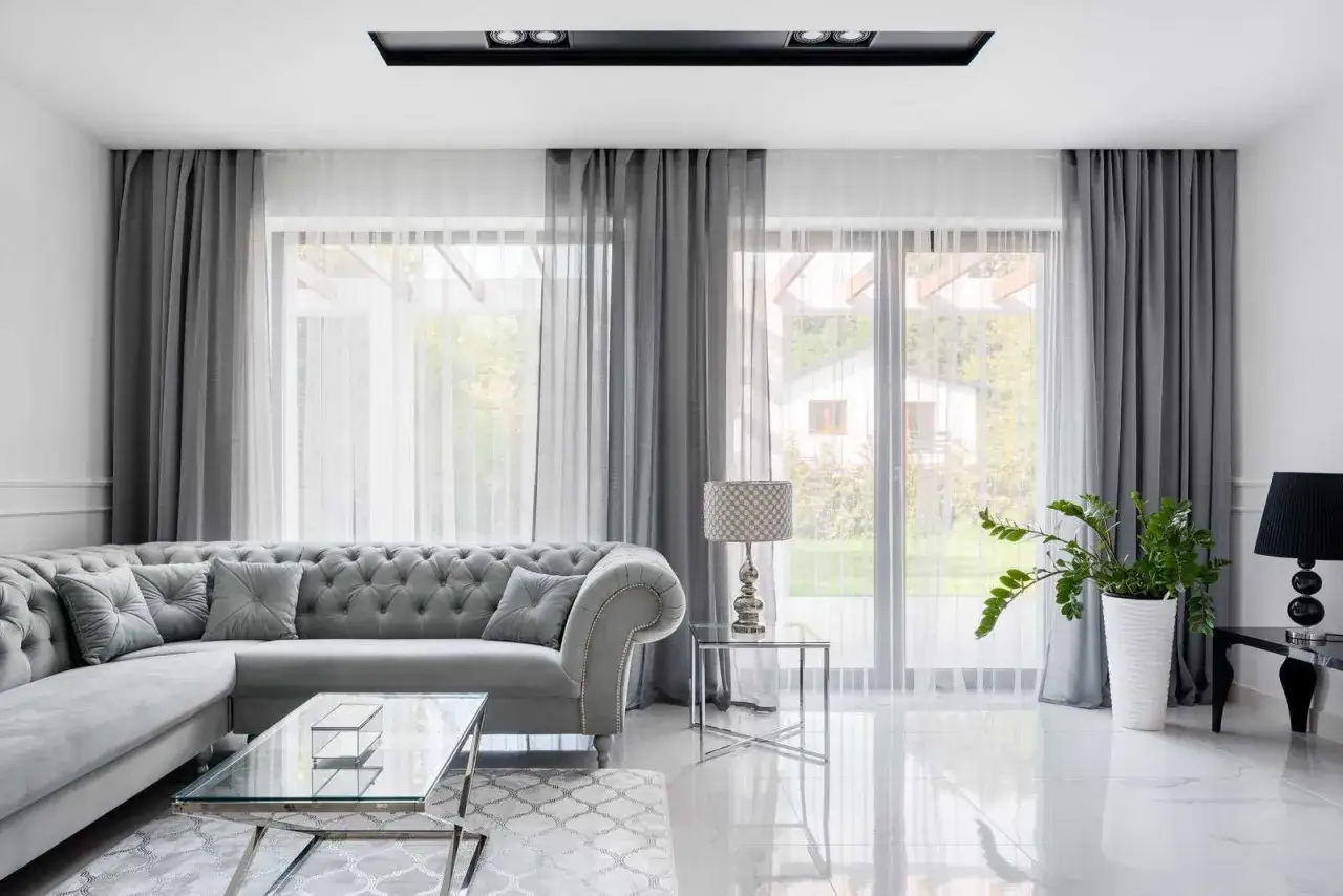 Eleganckie aranżacje okna w salonie: szara sofa, szklane stoliki i zasłony tworzą przytulną atmosferę.